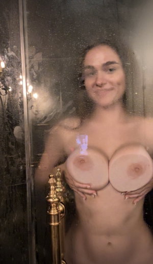 Brunette woman covering chest in steamy shower.