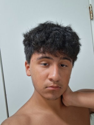 Shirtless man with curly dark hair, hand on neck, indoors against white door.