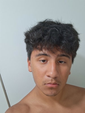Shirtless man with dark curly hair, looking at camera indoors.