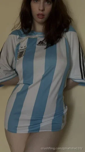 Woman in blue and white striped soccer jersey, standing indoors against plain wall.