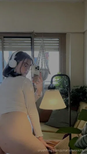 Woman in white long-sleeve crop top and beige leggings, taking mirror selfie in living room with