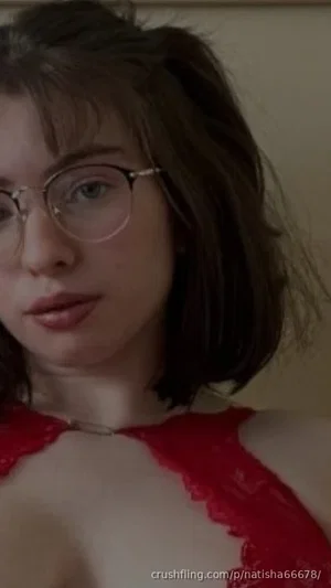 Woman with short brown hair and glasses wearing red lace top, indoor close-up.