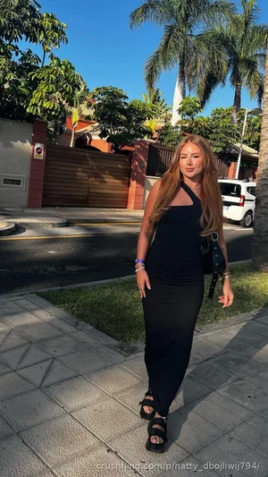 Woman in black dress walking on sidewalk outdoors near palm trees.