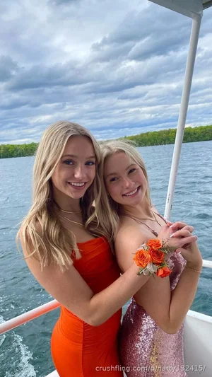 Two women in colorful dresses on a boat, smiling, with water and trees in background.