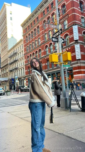 Woman in shearling coat and jeans standing on city street corner.