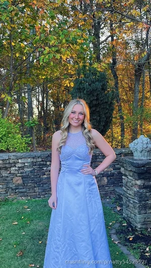 Blonde woman in a light blue formal gown standing outdoors in a garden with autumn trees.