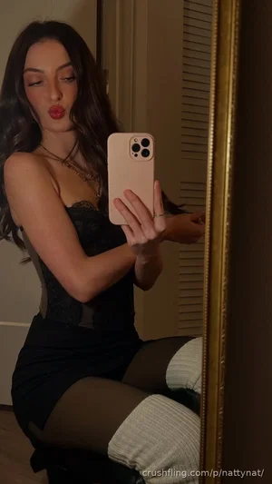 Woman in black lace top and thigh-high socks takes mirror selfie indoors.