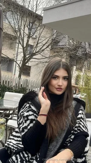 Woman with long brown hair in black and white patterned sweater, sitting outdoors near patio