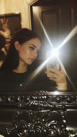 Woman with dark hair taking mirror selfie in black top.