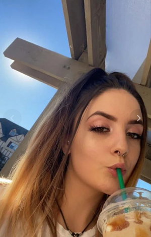 Woman with long hair sipping drink outdoors under beams.