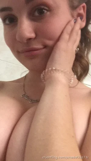 Woman with bare shoulders and chest, wearing necklace, hand on face, indoor setting.