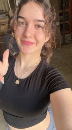 Woman with wavy hair in black crop top and jeans, smiling in indoor setting.
