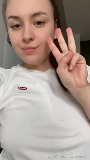 Woman in white t-shirt making peace sign, indoor setting.