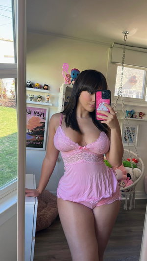 Woman in pink lingerie taking mirror selfie in bedroom.