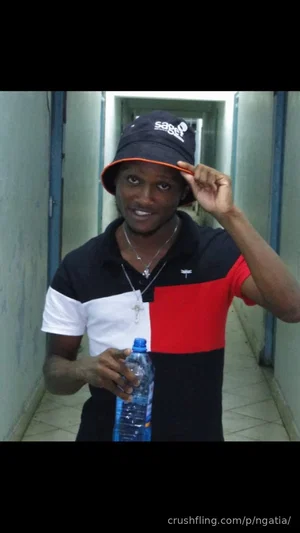 Man in black, white, and red polo shirt and bucket hat holding water bottle in hallway.