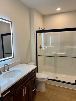 Modern bathroom with white vanity, dark wood cabinets, glass shower enclosure, and illuminated