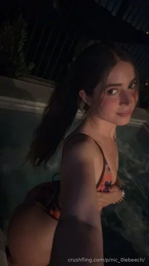 Woman in floral bikini taking selfie in pool at night, dark hair, outdoor setting.