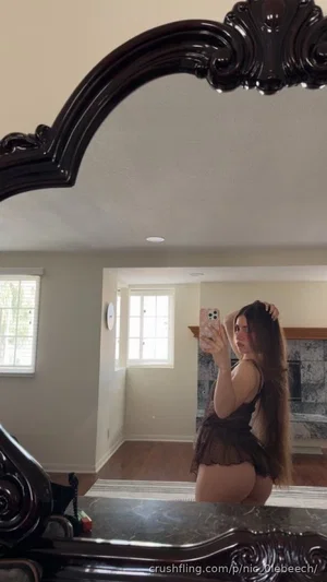 Woman in black lace lingerie taking mirror selfie in bedroom.
