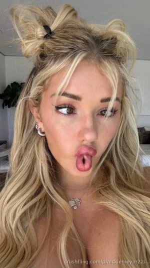 Blonde woman with long hair, making a playful face, topless, indoors.