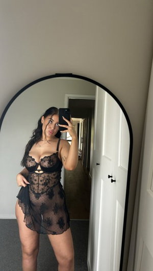 Curvy woman in black lace lingerie taking mirror selfie indoors.
