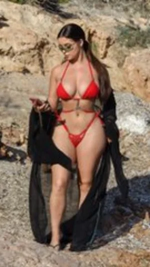 Woman in red bikini and black sheer fabric standing on rocky terrain.