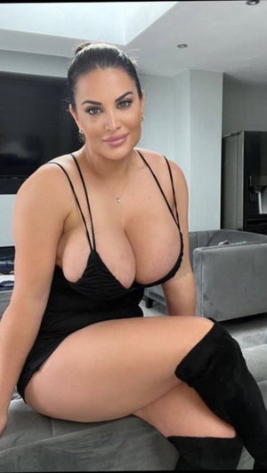 Curvy woman in black dress sitting indoors on couch.