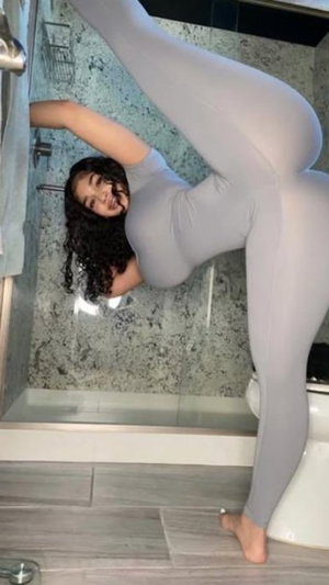 Curvy woman in gray bodysuit posing in bathroom.