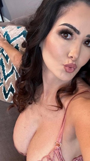 Woman with dark hair in pink lingerie posing on couch indoors.