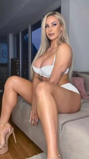 Blonde woman in white lingerie sitting on a couch indoors.