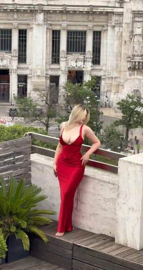 Blonde woman in red dress posing on city balcony.