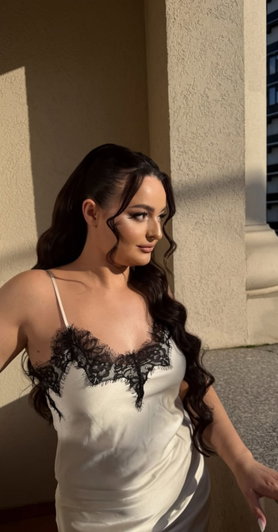 Woman with long dark hair in white lace dress outdoors.