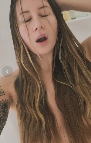 Woman with long wet hair and arm tattoos in bathroom.