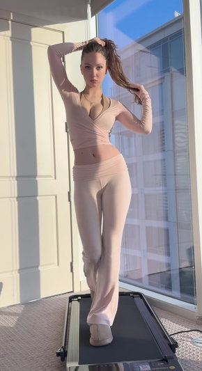 Woman in beige activewear posing on treadmill by window.