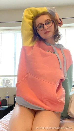 Woman in colorful hoodie, sitting on bed, wearing glasses, indoors.