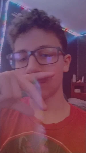 Young person with curly hair and glasses wearing a red shirt indoors.