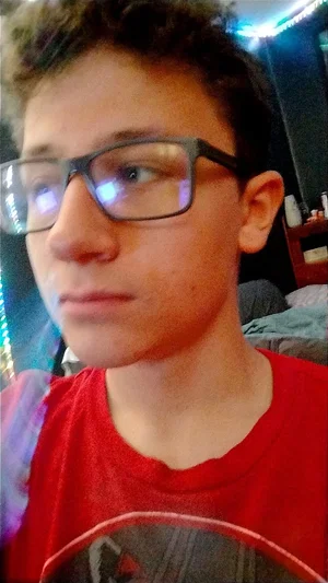 Young man with curly hair and glasses wearing a red t-shirt indoors.