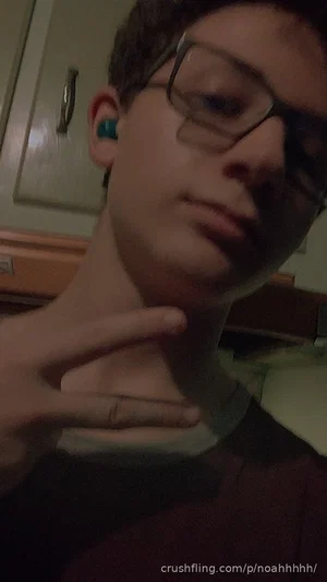 Young man with glasses and earbuds making a peace sign indoors.