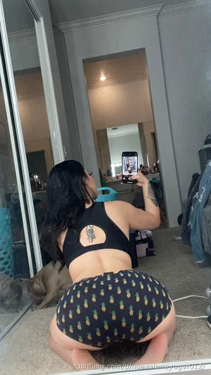 Woman in black crop top and pineapple-print shorts taking mirror selfie in bedroom.