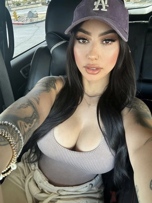 Woman with long dark hair and tattoos wears striped top and cap, sitting in car.
