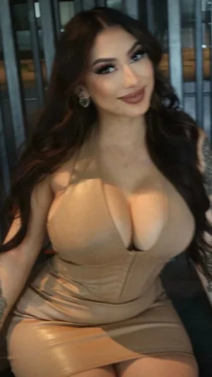 Woman with long dark hair in a tight beige dress, posing indoors.