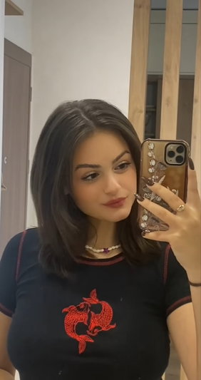 Woman with dark hair in black t-shirt with red fish design, taking mirror selfie indoors.