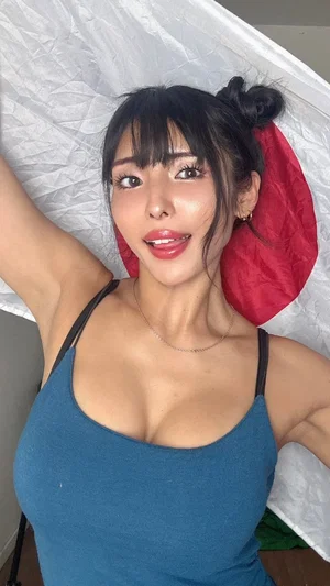 Woman with dark hair in bun, wearing blue tank top, lying on bed with white and red bedding.