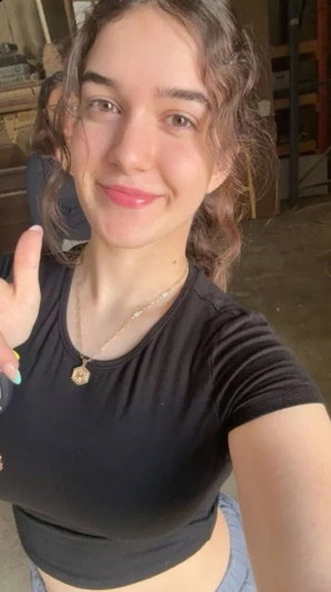 Woman with brown hair in black crop top taking indoor selfie.