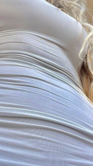 Blonde woman in white ribbed top, close-up of torso and shoulder.