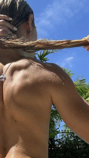 Woman with wet back and long hair outdoors under blue sky, showing bare shoulders and back.