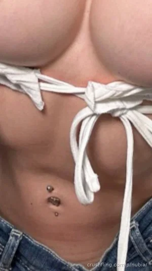 Woman with curvy body wearing white string top and jeans, showing midriff and belly button piercing.