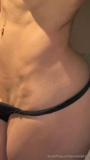 Woman in black thong, showing toned midriff and hips, indoor setting.