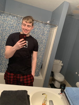 Man taking mirror selfie in bathroom wearing black t-shirt and plaid pants.