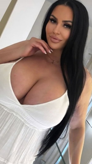 Woman with long black hair in white top posing indoors.