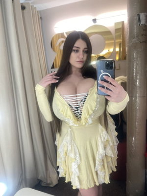 Woman in yellow lace dress with long dark hair taking mirror selfie indoors.